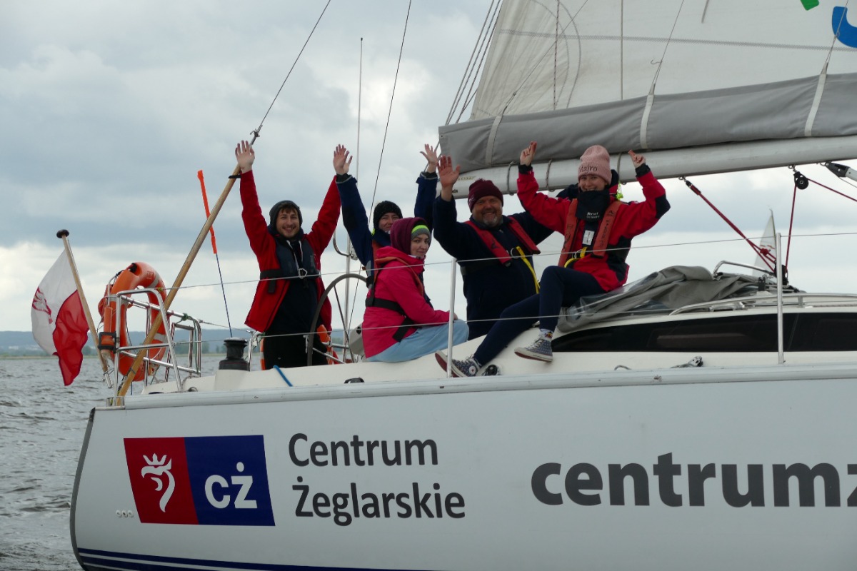 załoga jachtu unosi ręce w górę i macha do obiektywu fotografa